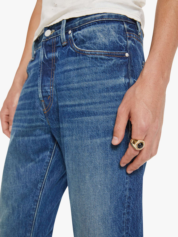Close up view of a man in a mid blue jean with a standard straight leg with a mid rise, button fly and 32-inch inseam with a clean hem.