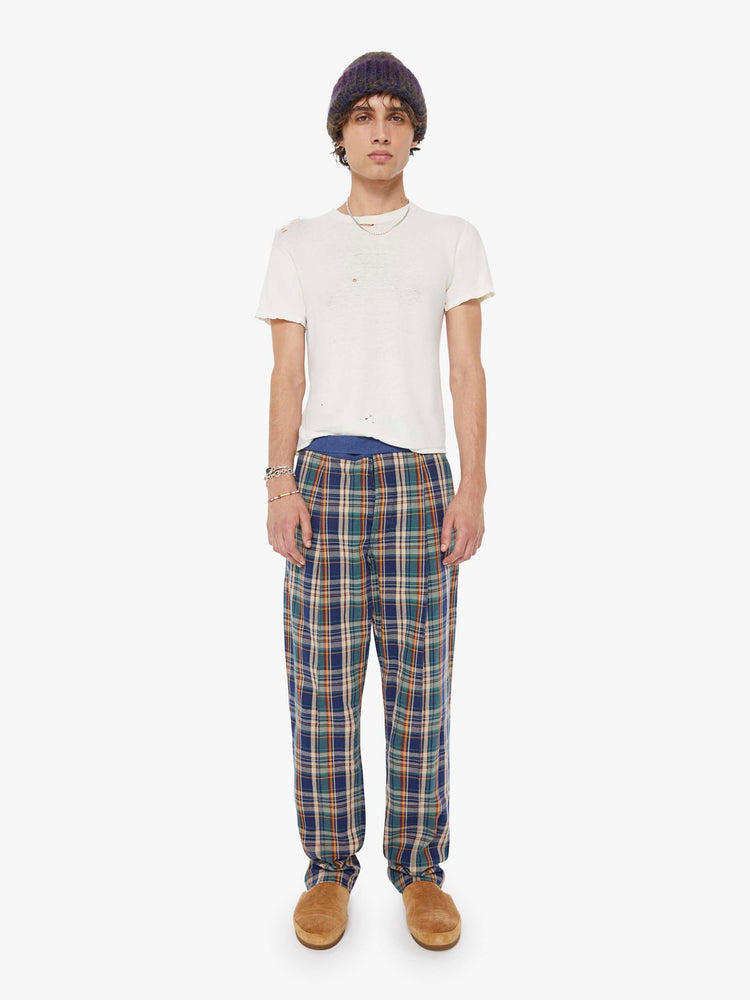 Front view of a man in a navy, orange plaid  pant with a mid rise, zip fly and loose leg. It's detailed with slit pockets and front pleats. 