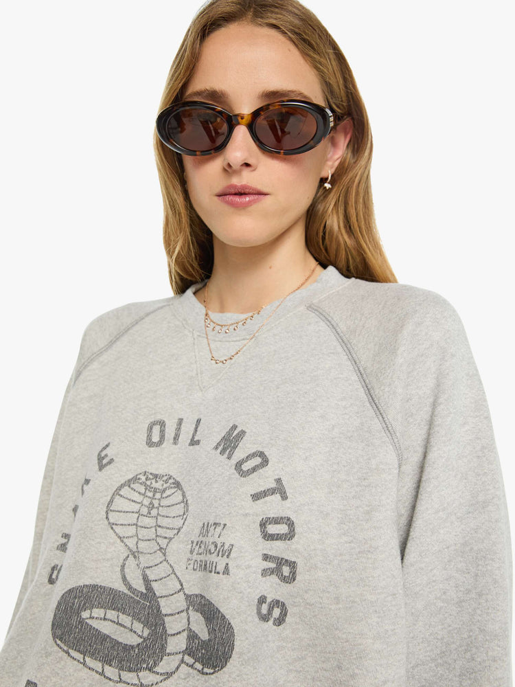 WOMAN close up view heathered light grey sweatshirt features a faded snake graphic and block text on the front.