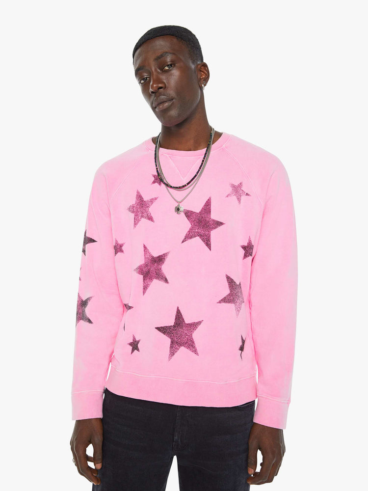 Front view of a man in bright pink sweatshirt with black stars printed across the body and one sleeve.