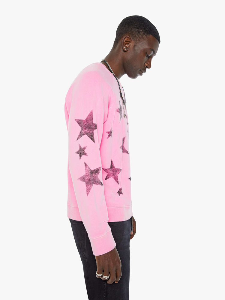 Side view of a man in bright pink sweatshirt with black stars printed across the body and one sleeve.