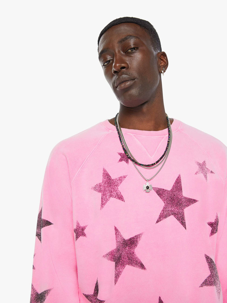 Close up view of a man in bright pink sweatshirt with black stars printed across the body and one sleeve.