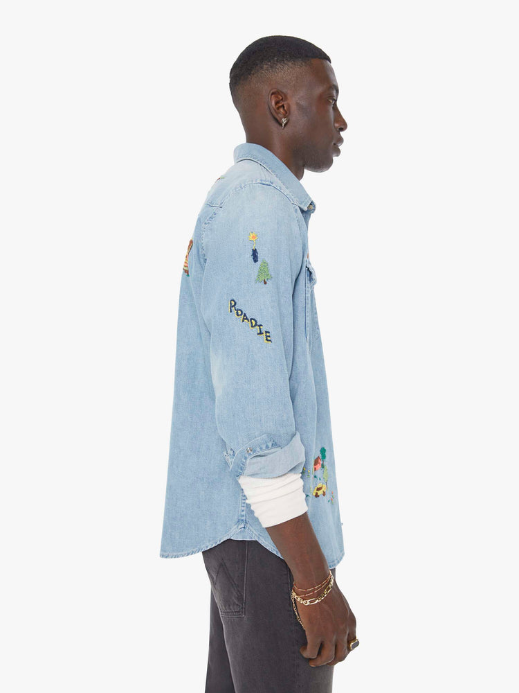 Side view of a man in a light blue denim button up with fading and colorful embroidery throughout.