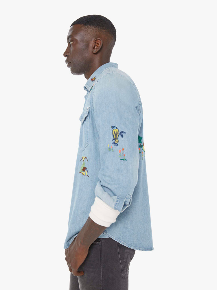 Left side view of a man in a light blue denim button up with fading and colorful embroidery throughout.