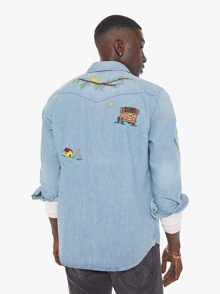 Back view of a man in a light blue denim button up with fading and colorful embroidery throughout.