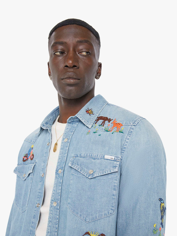 Close up view of a man in a light blue denim button up with fading and colorful embroidery throughout.