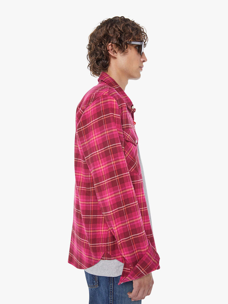 Side view of a man in a hot pink and red plaid print classic button down shirt with flap patch pockets, long sleeves and a curved hem.