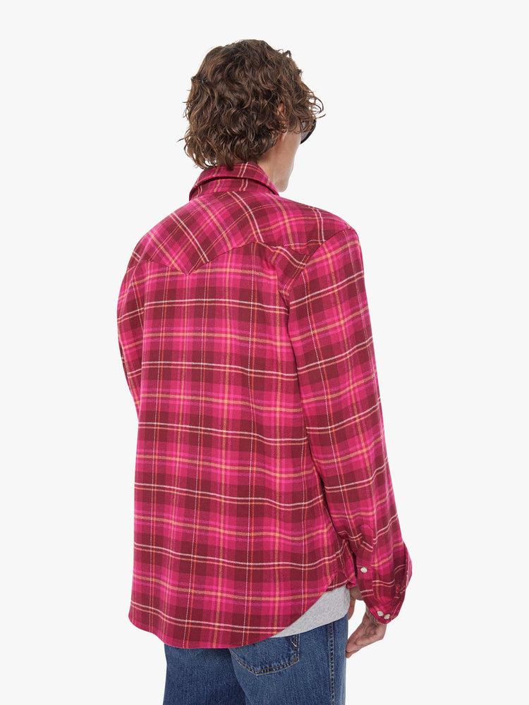 Back view of a man in a hot pink and red plaid print classic button down shirt with flap patch pockets, long sleeves and a curved hem.