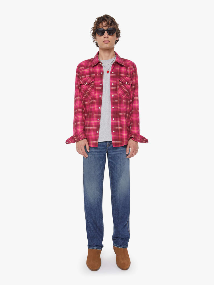 Full body view of a man in a hot pink and red plaid print classic button down shirt with flap patch pockets, long sleeves and a curved hem.
