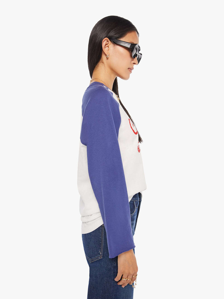 WOMAN side view in a  baseball tee with a crew neck, 3/4-length frayed sleeves and a curved hem in white with blue sleeves and a red demolition derby graphic on the front.