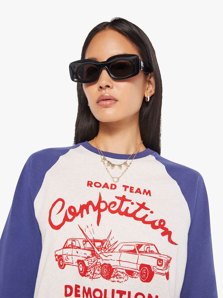 WOMAN close up view in a  baseball tee with a crew neck, 3/4-length frayed sleeves and a curved hem in white with blue sleeves and a red demolition derby graphic on the front.