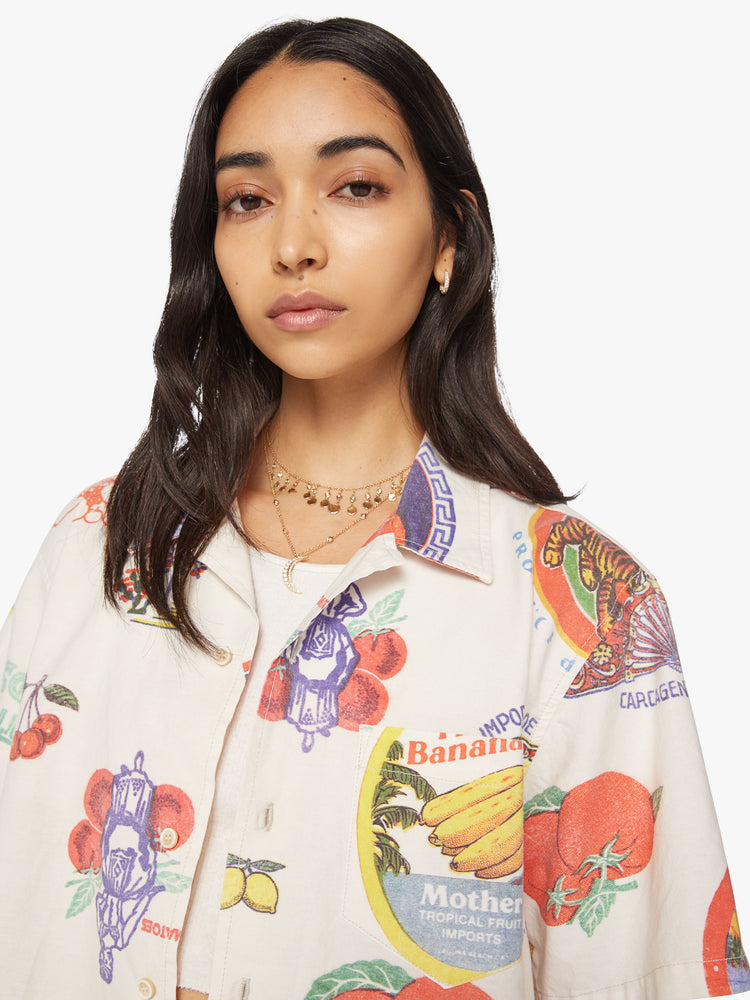 WOMEN close up view  short sleeve button-up with a patch pocket and slightly cropped hem in off white color with images of fruit labels.