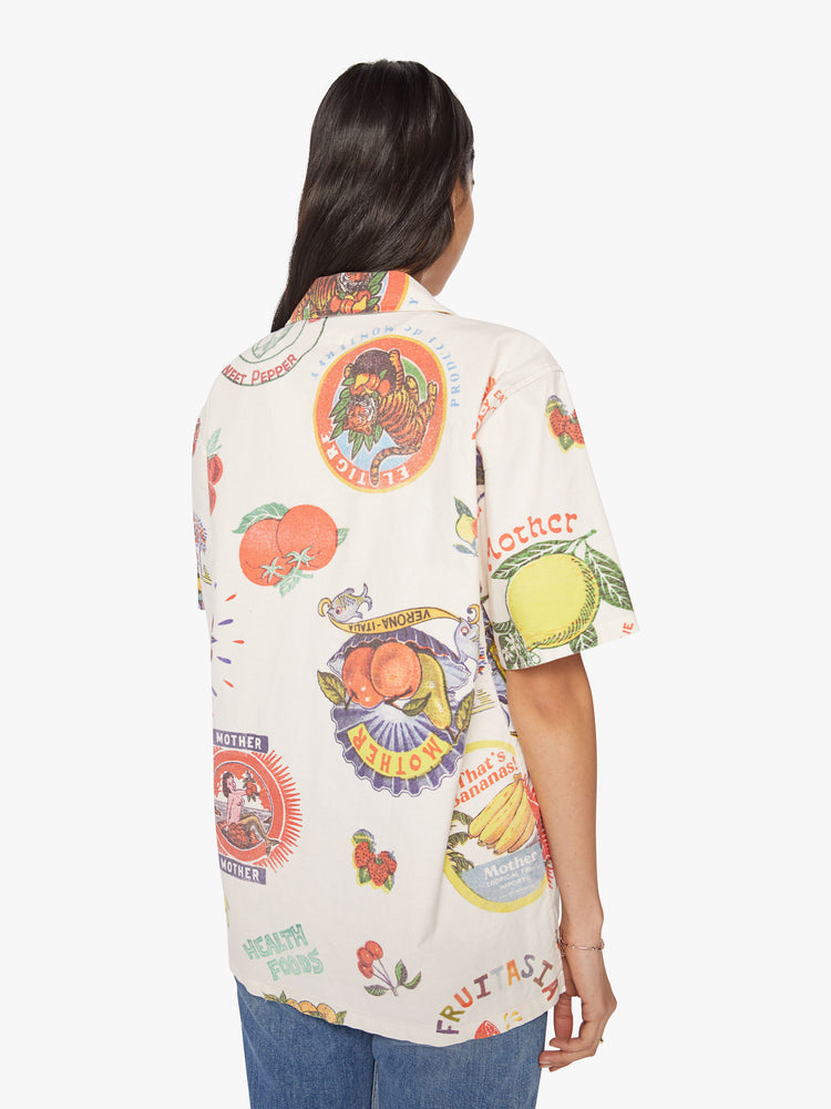 WOMEN back view short sleeve button-up with a patch pocket and slightly cropped hem in off white color with images of fruit labels.