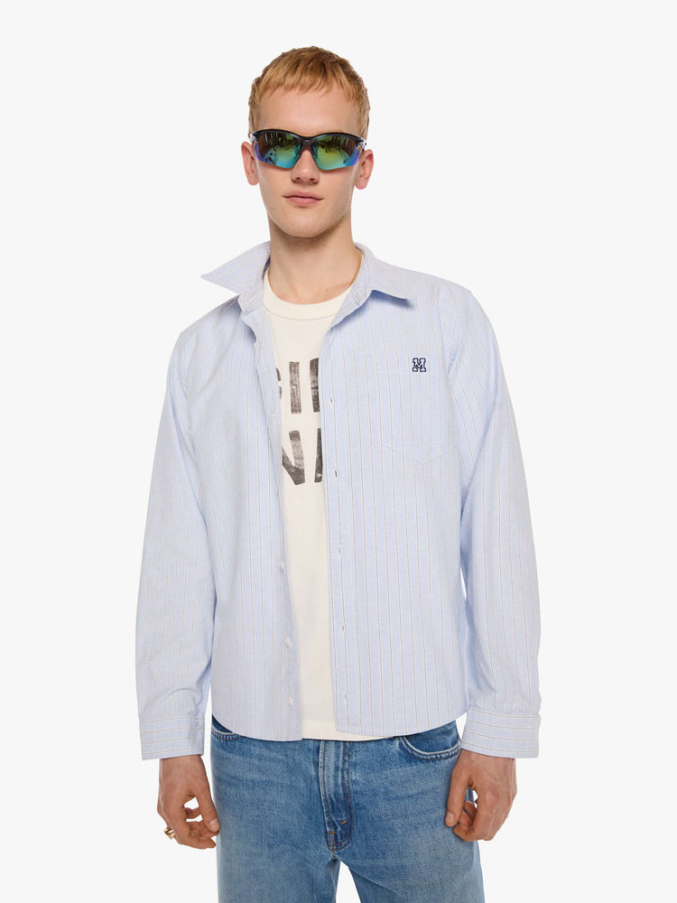 Front view of a man in light blue shirt with off white and black stripes and a navy M embroidered on the chest.