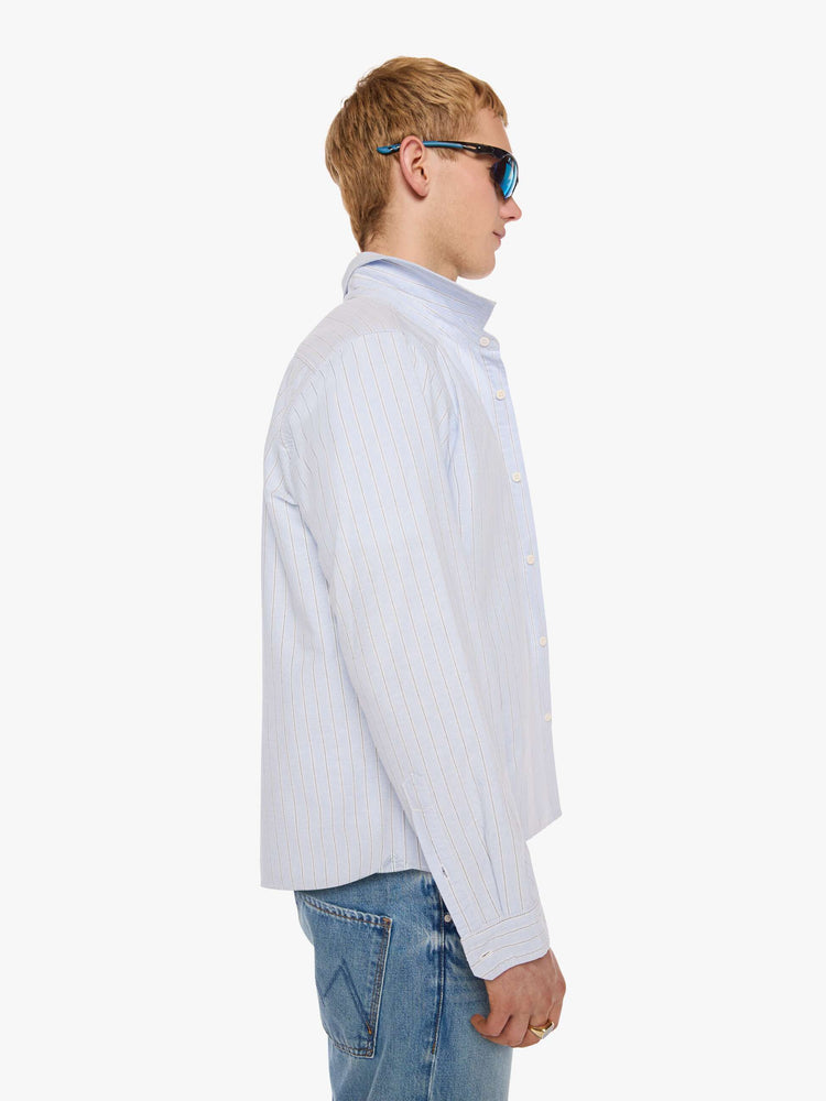 Side view of a man in light blue shirt with off white and black stripes and a navy M embroidered on the chest.