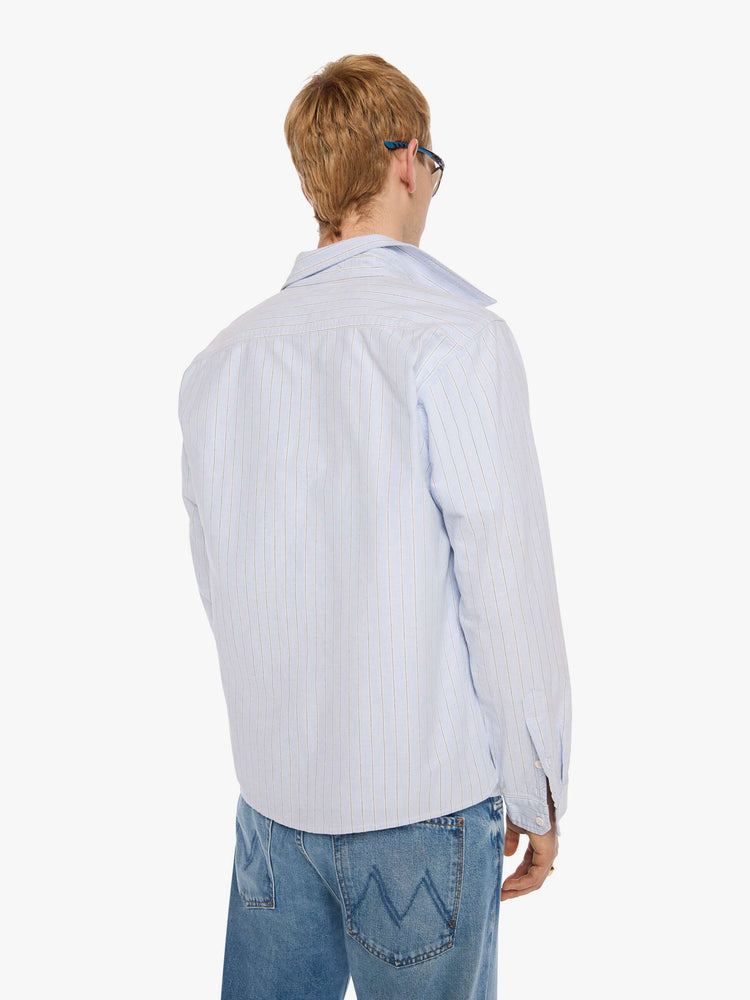 Back view of a man in light blue shirt with off white and black stripes and a navy M embroidered on the chest.