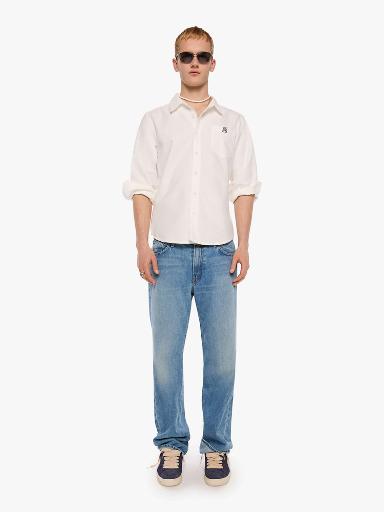 Full body view of  man in the top is designed in white with a navy M embroidered on the chest.