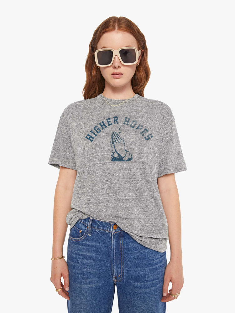WOMEN front view of a woman in a heather grey unisex crew neck tee featuring a faded blue graphic of hands of the words "HIGHER HOPES".