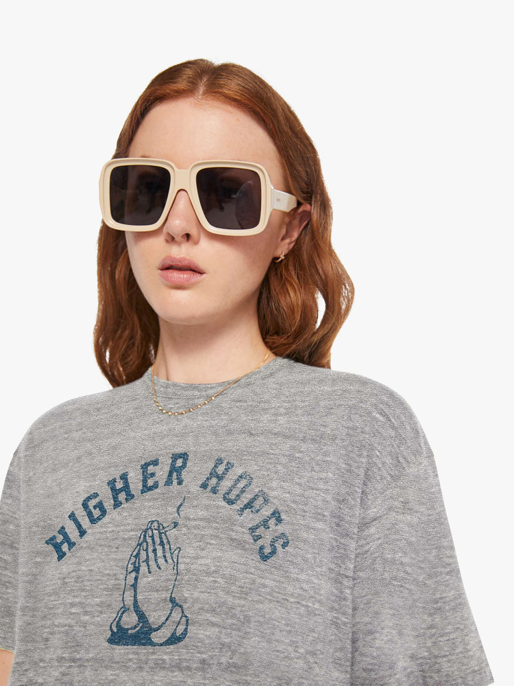 WOMEN close up detail front view of a woman in a heather grey unisex crew neck tee featuring a faded blue graphic of hands of the words "HIGHER HOPES".