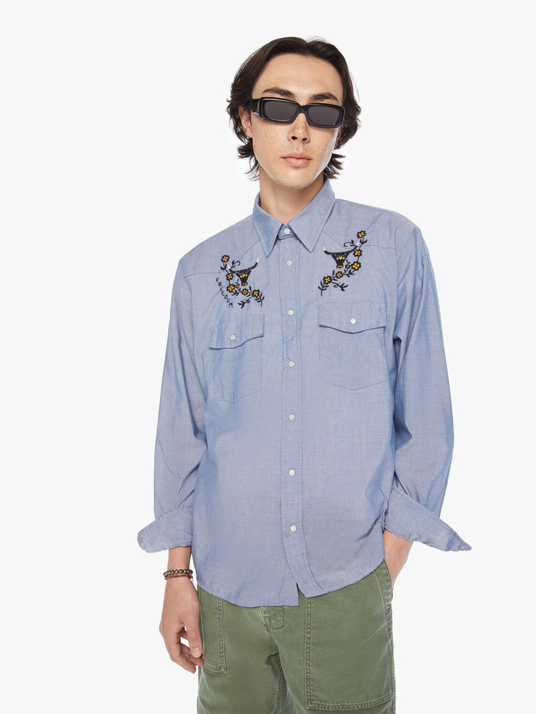 Front view of a men classic long sleeve button-up with Western-inspired patch pockets in a light blue hue with embroidered bulls, flowers and text on the chest.