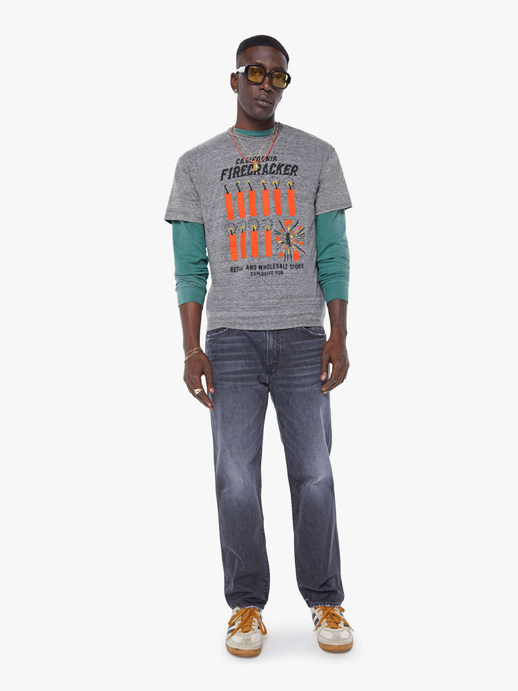 MEN full body view in an oversized tee in heathered grey, the tee features a firecracker graphic in red and black on the front.