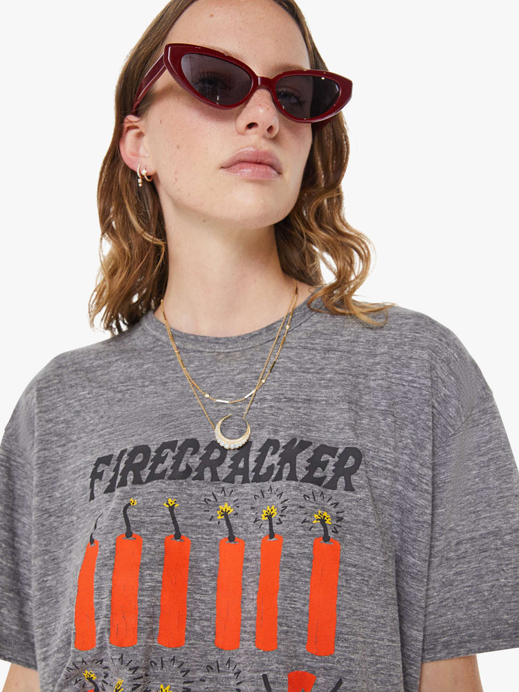 WOMAN close up view in an oversized tee in heathered grey, the tee features a firecracker graphic in red and black on the front.