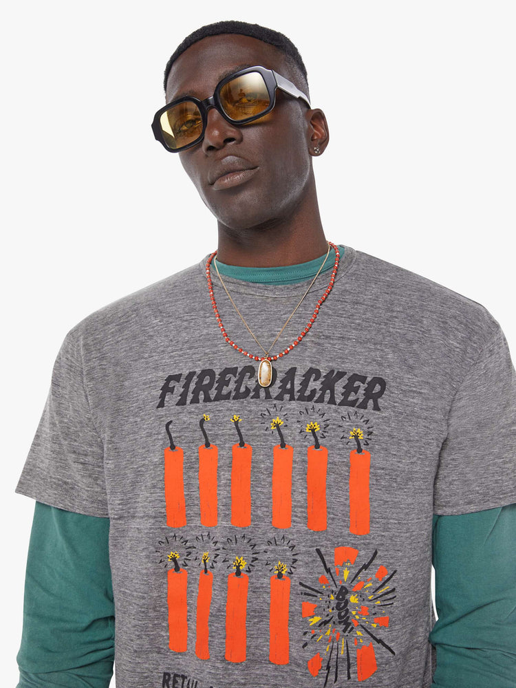 MEN close up view in an oversized tee in heathered grey, the tee features a firecracker graphic in red and black on the front.