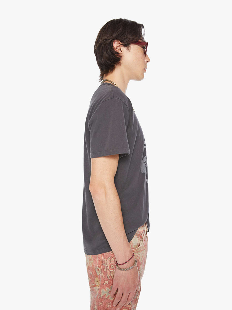 Side view of a men oversized tee with drop shoulders and a loose fit in a faded black tee with a faded sun hat graphic and text.