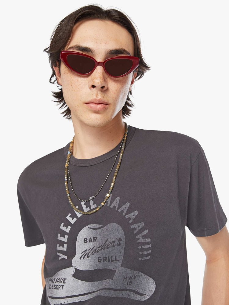Close up view of a men oversized tee with drop shoulders and a loose fit in a faded black tee with a faded sun hat graphic and text.