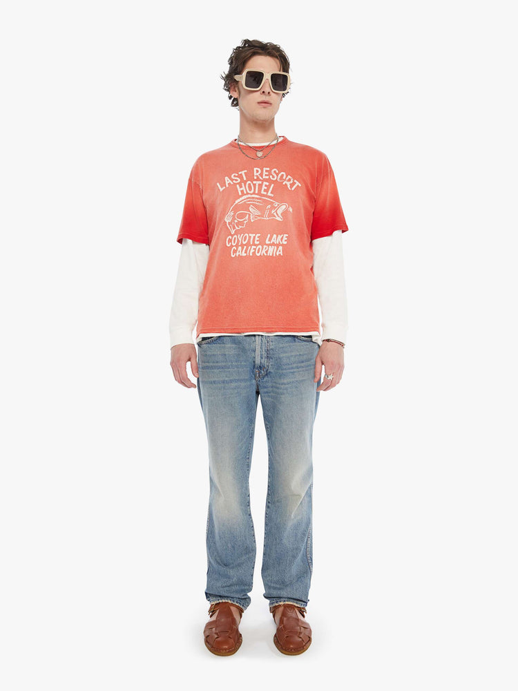 MEN full body view in an oversized tee in a red wash with an off-white graphic inspired by an old-school hotel logo.