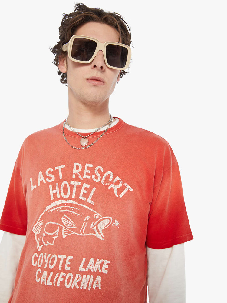 MEN close up view in an oversized tee in a red wash with an off-white graphic inspired by an old-school hotel logo.