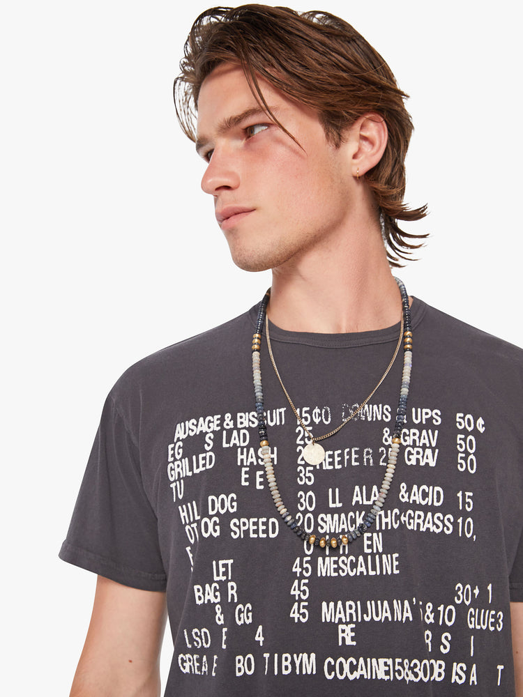Close up view of a men oversized tee with drop shoulders and a loose fit in a dark grey hue with a menu of illicit substances on the front.