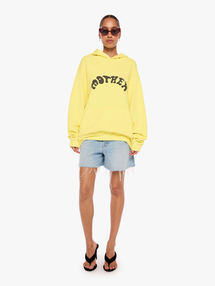 WOMAN full body view of a yellow hoodie features MOTHER's name in dark grey across the front.