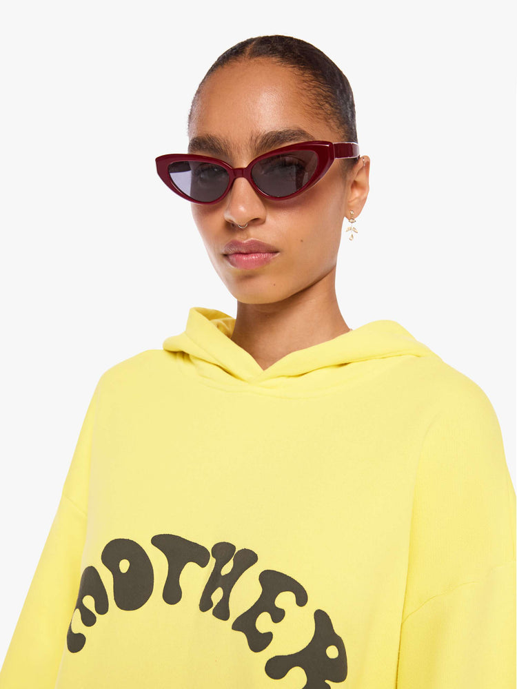 WOMAN close up view of a yellow hoodie features MOTHER's name in dark grey across the front.