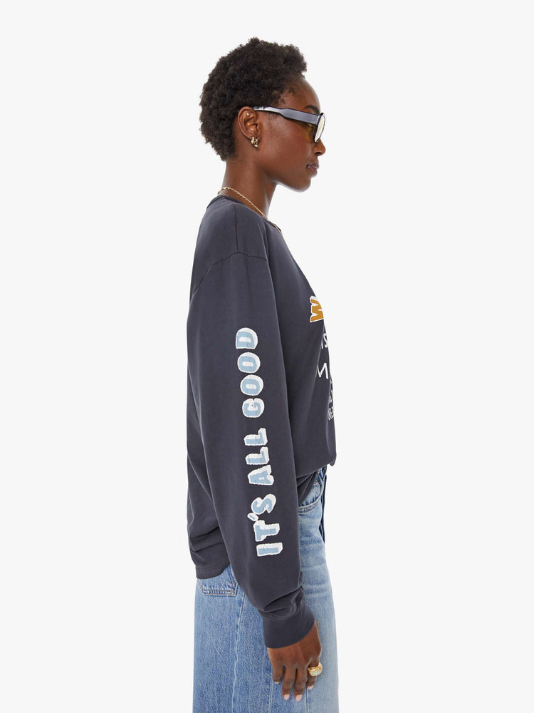 WOMAN side view of a faded black long sleeve tee features a yellow and white text graphic on the front inspired by a vintage mountaineering team shirt.