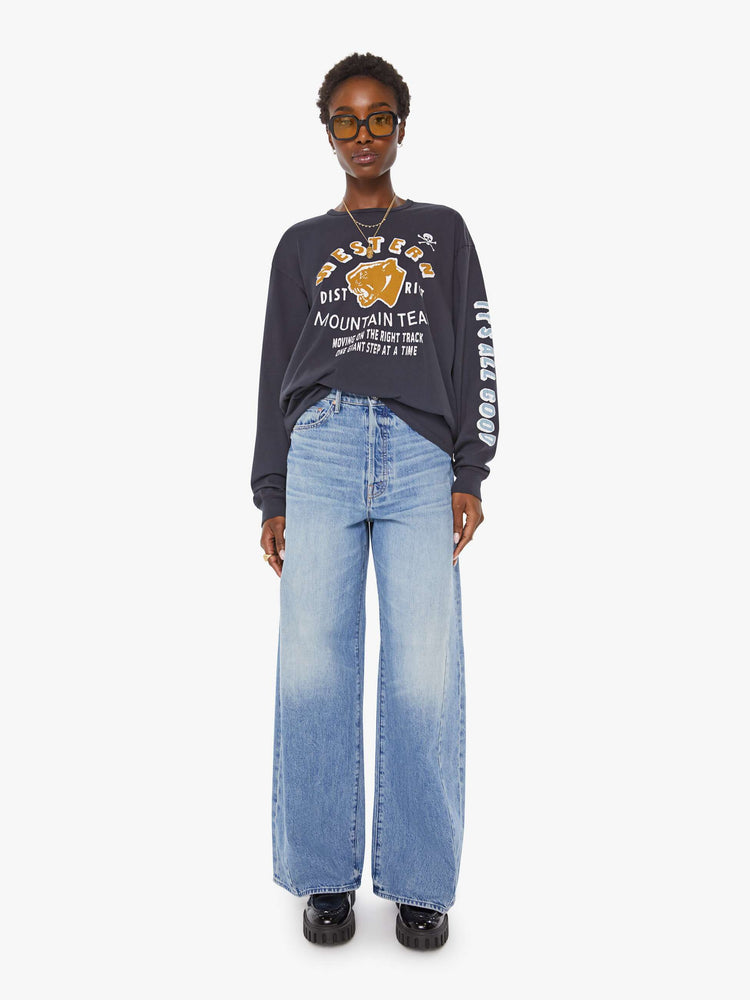 WOMAN full body view of a faded black long sleeve tee features a yellow and white text graphic on the front inspired by a vintage mountaineering team shirt.