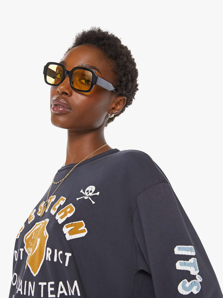 WOMAN close up view of a faded black long sleeve tee features a yellow and white text graphic on the front inspired by a vintage mountaineering team shirt.