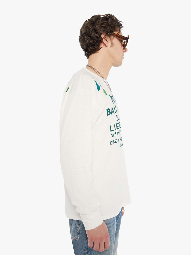MEN side view of rugby style tee in off white with a green text graphic on the front and colorful lures across the shoulders.