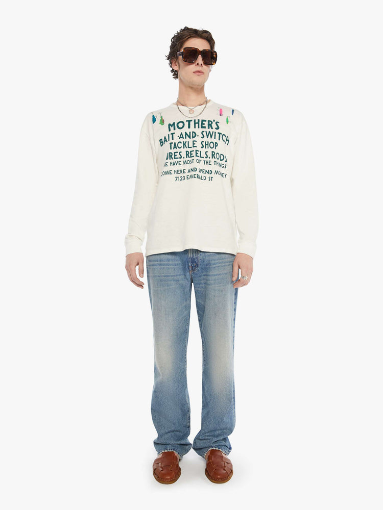 MEN full body view of rugby style tee in off white with a green text graphic on the front and colorful lures across the shoulders.