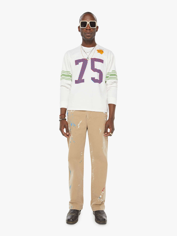 MEN full body view in a white rugby-style tee with a crew neck, long sleeves with a checkered "75" graphic on the front, mint-green stripes on the sleeves and a tiger near the neck.