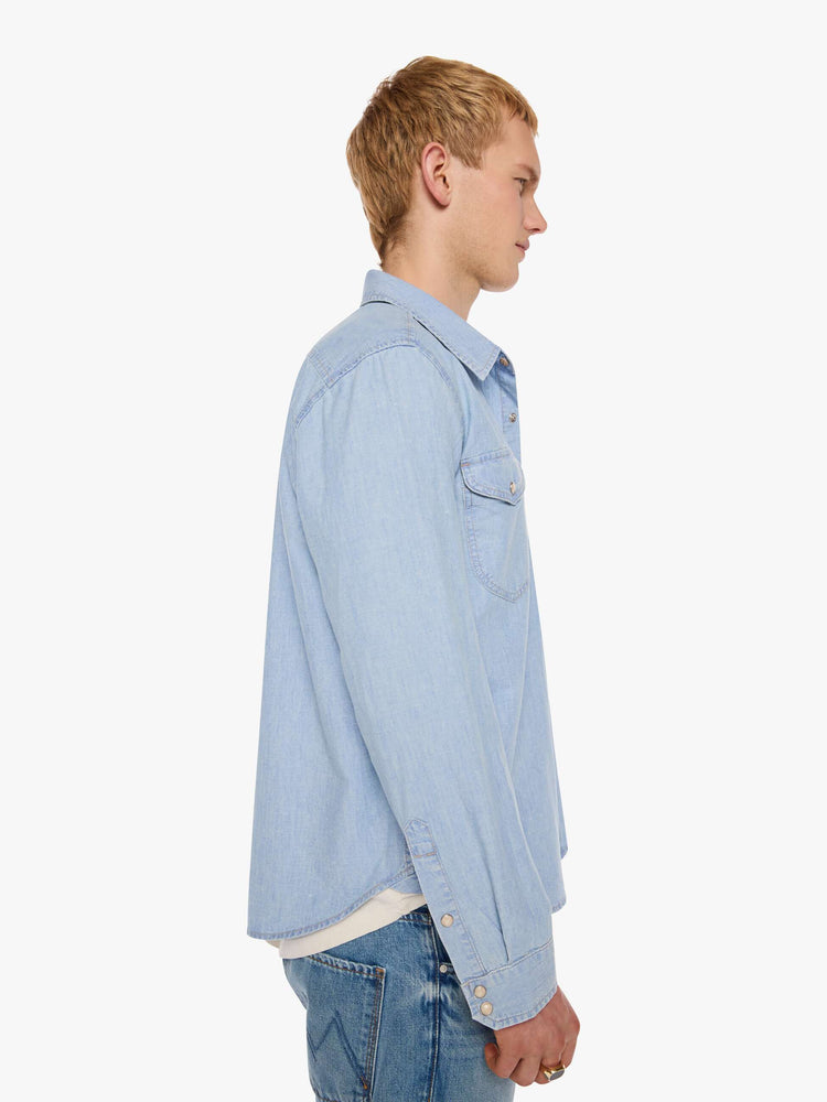 Side view of a man in a light blue   button-up shirt with front patch pockets and a slightly curved hem. 