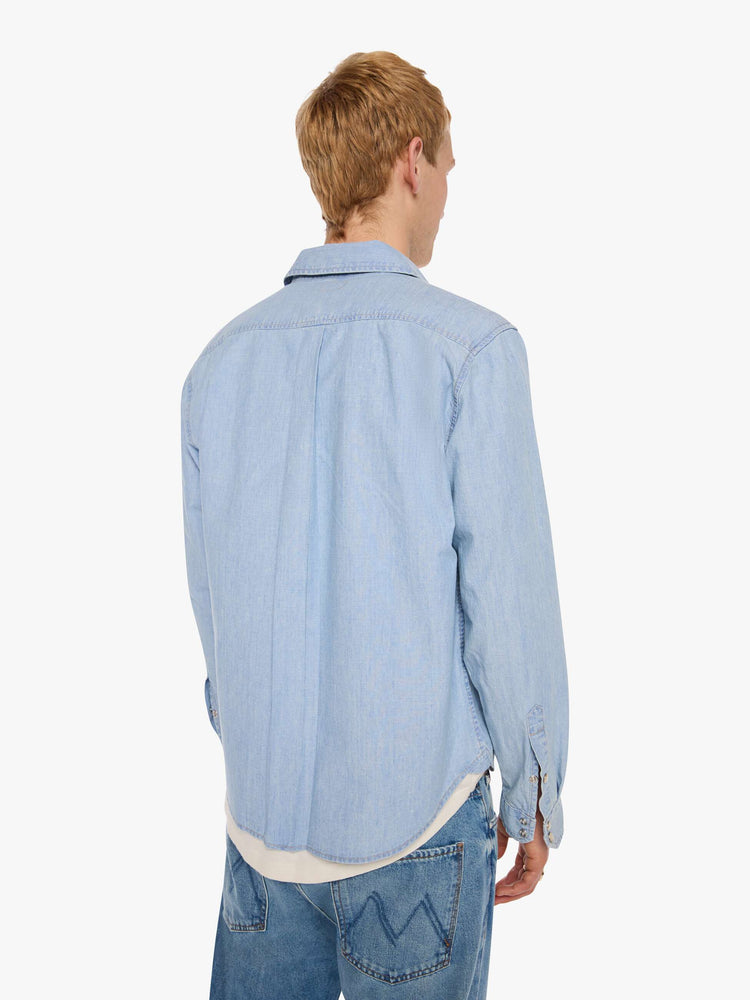 Back view of a man in a light blue   button-up shirt with front patch pockets and a slightly curved hem. 