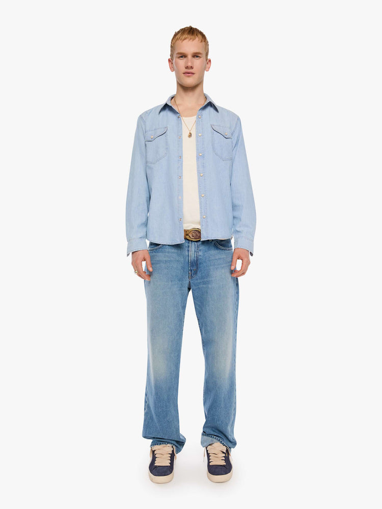 Full body view of a man in a light blue   button-up shirt with front patch pockets and a slightly curved hem. 
