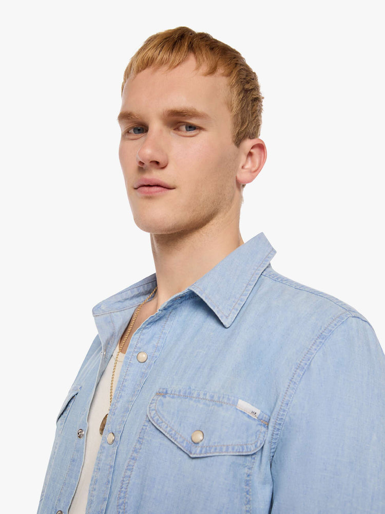 Close up view of a man in a light blue   button-up shirt with front patch pockets and a slightly curved hem. 