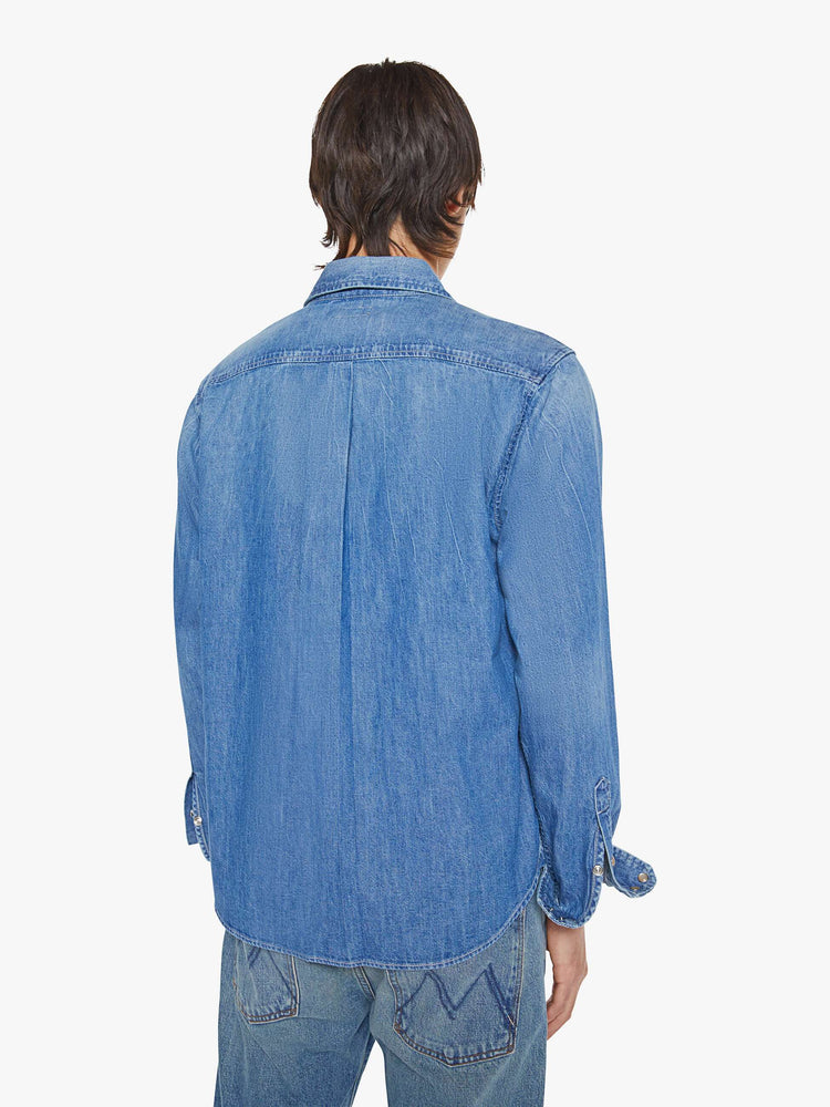 Back view of a man in a vintage blue button-up with front patch pockets and a slightly curved hem.