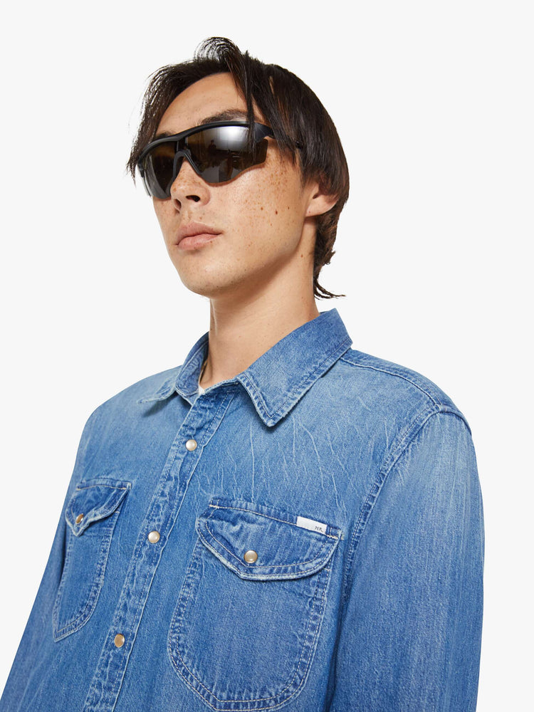 Close up view of a man in a vintage blue button-up with front patch pockets and a slightly curved hem.