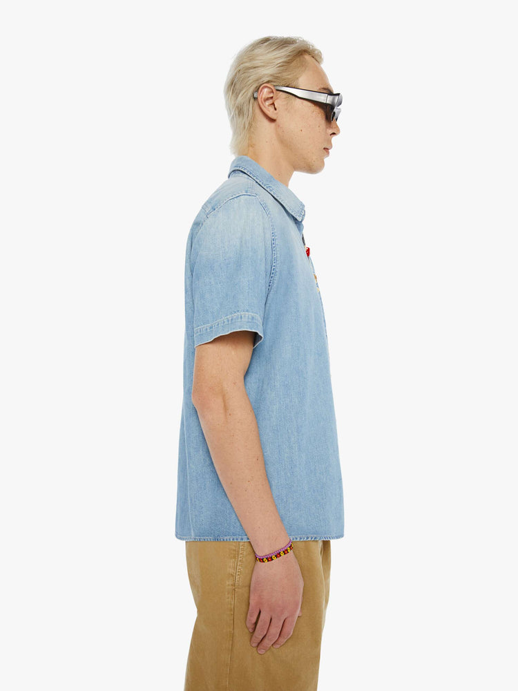 Side view of a man in a light blue short-sleeve collared button-up with a patch pocket and a straight hem.