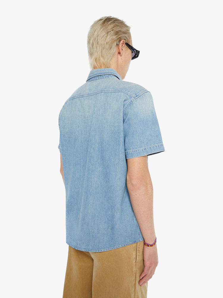 Back view of a man in a light blue short-sleeve collared button-up with a patch pocket and a straight hem.