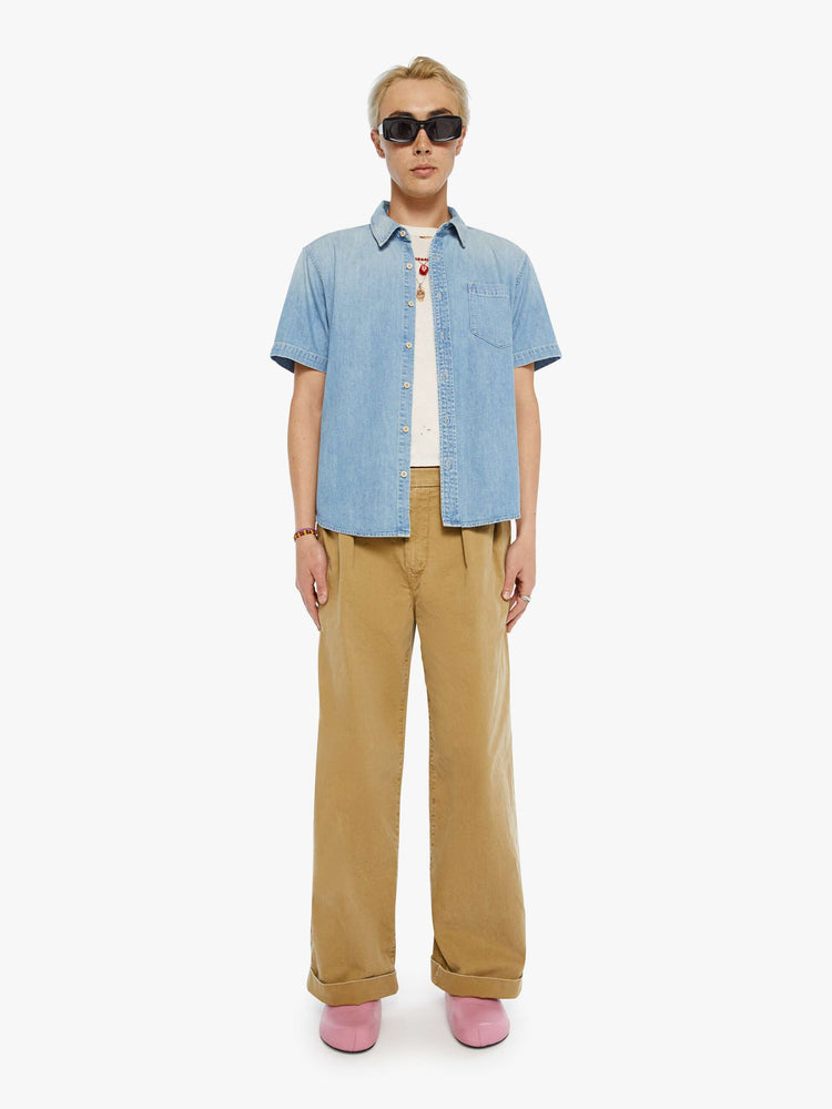 Full body view of a man in a light blue short-sleeve collared button-up with a patch pocket and a straight hem.