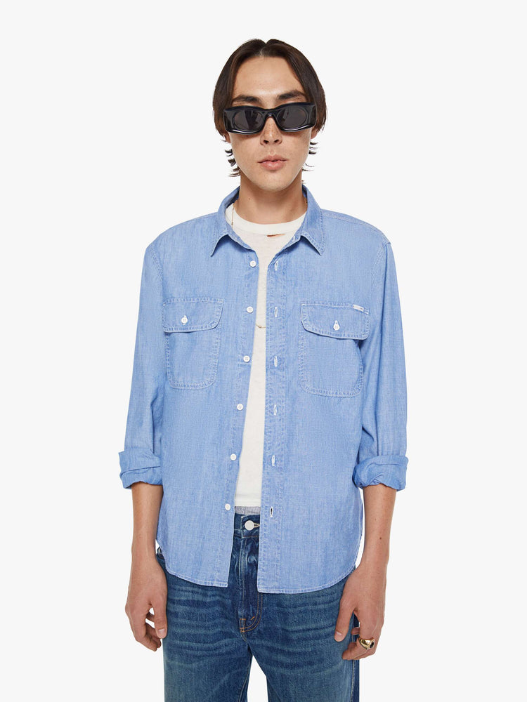 Front view of a man in a light blue denim button-up with patch pockets, long sleeves and a curved hem.